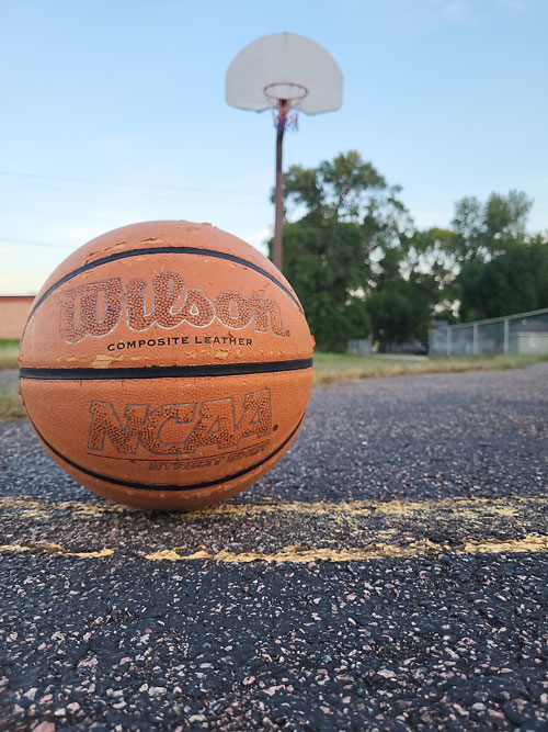 A closeup of a basketball on the ground with a hoop in the background.