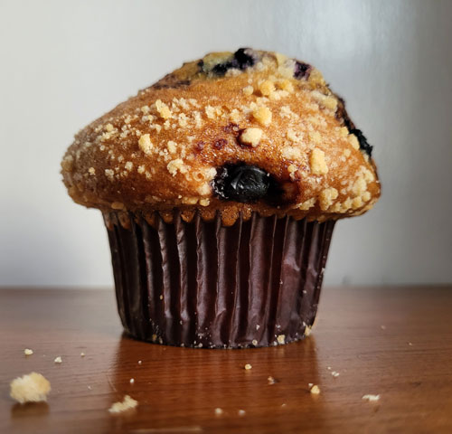Close-up of a blueberry muffin resting on a wooden table.
