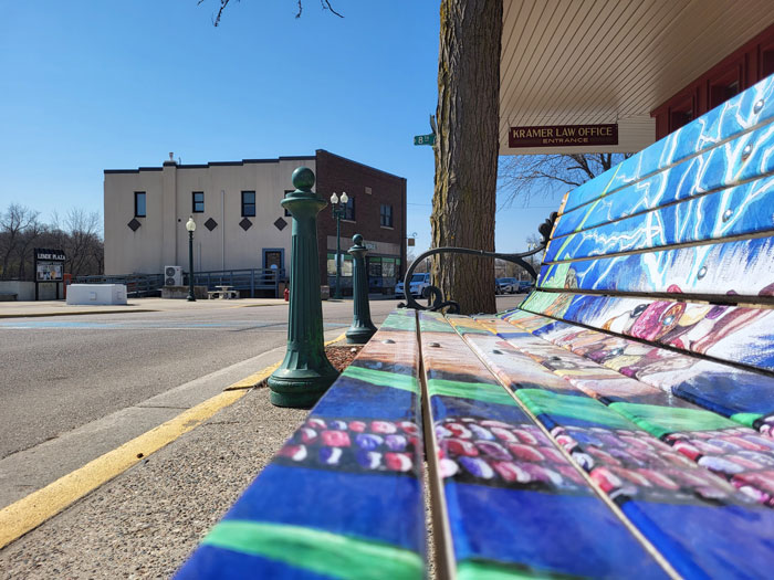 A colorful bench next to a street.