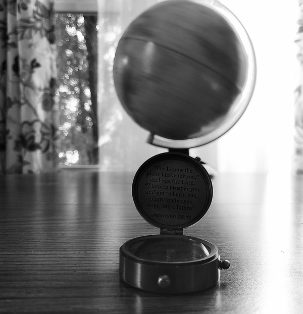 A black and white photo of a compass on a wooden table with a spinning globe behind.