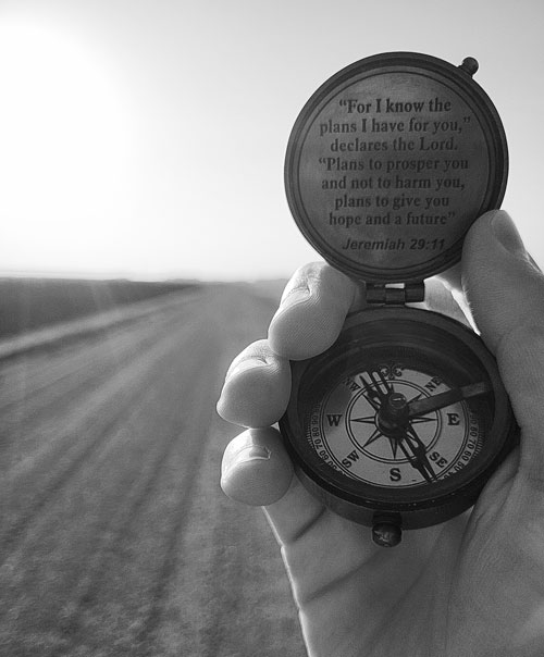 A black and white photo of a person holding a compass on a dirt road.