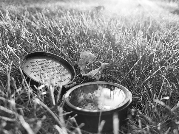 A black and white photo of a compass on the ground, facing up towards the sunlight.