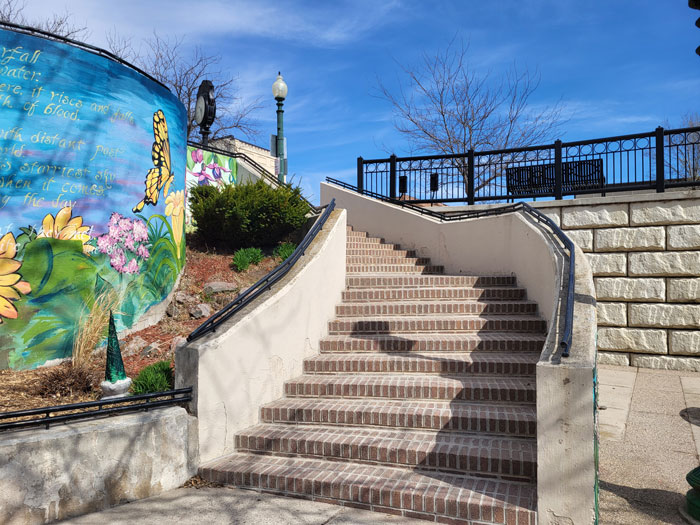 A brick stairway leading up, with a blue sky in the background and a colorful, painted wall on the side.