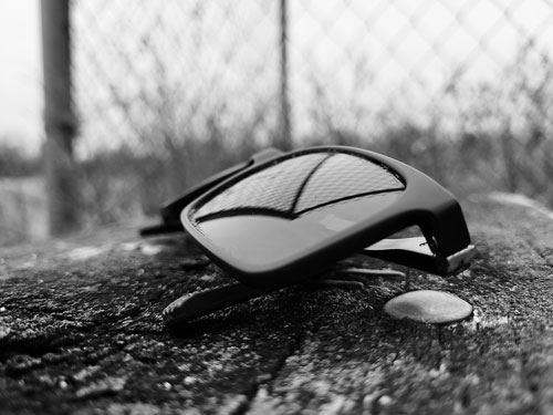 A close-up of a pair of sunglasses laying on a wooden bench next to a fence.