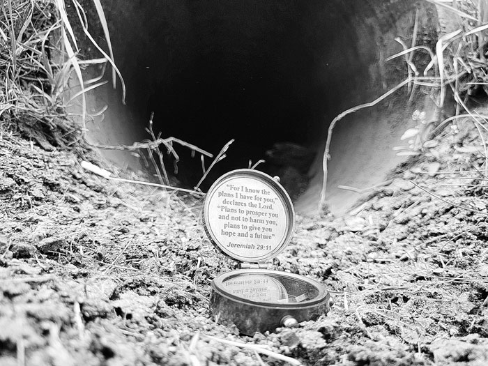 A black and white photo of a compass in front of a drainage pipe.
